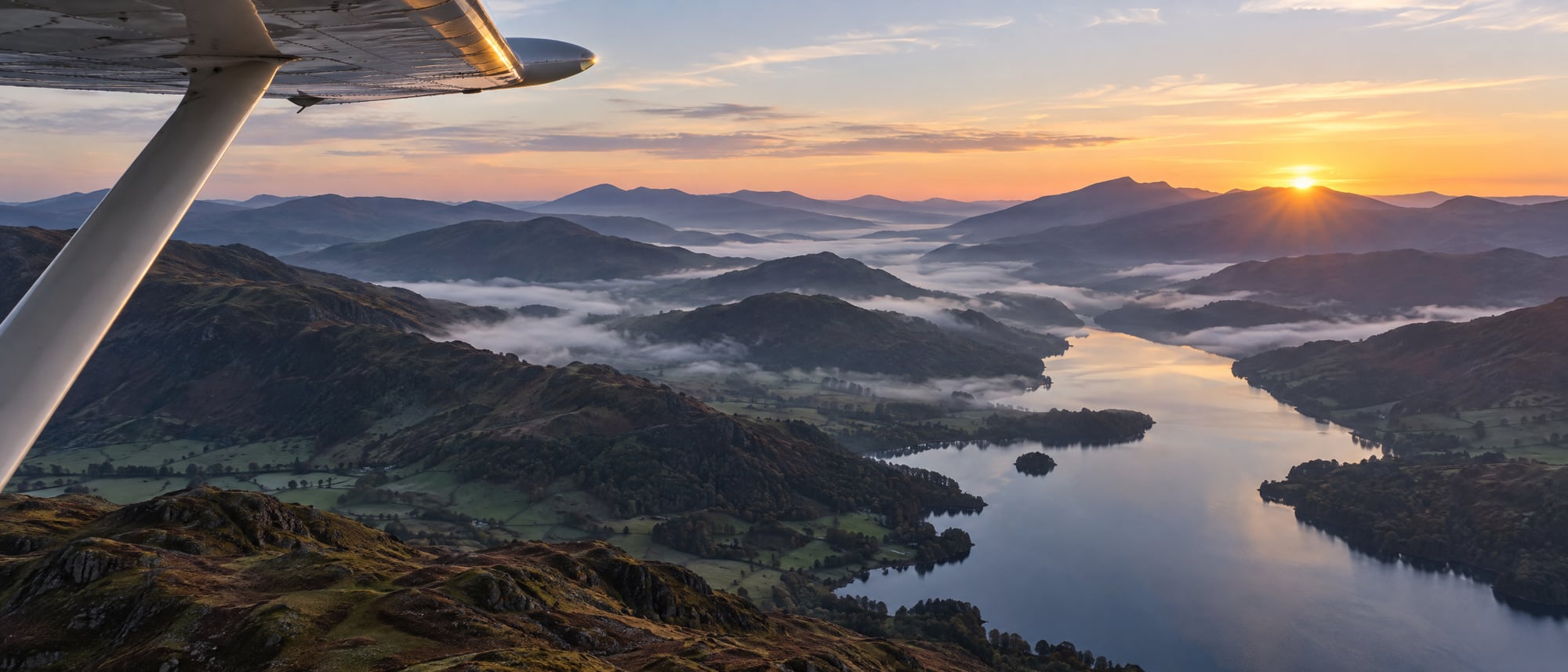 Dawn over the Lake District from the cockpit, a wingtip in frame, printed as a navy halftone.